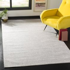 a yellow chair sitting on top of a black floor next to a white rug in a living room