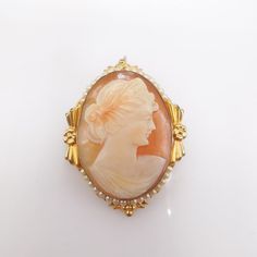 This beautiful carving, done crisply in shell, is framed by an Art Deco embellished vermeil (gold over silver) frame. Tiny seed pearls accent the top and bottom points of the carving. The back has a safety clasp, where the pin is held in place by tension and secured with a rolling metal bit, and a hidden bail sits at the top -- enabling the piece to be worn on a chain as a necklace.MEASUREMENTS: 1.5" x 1.2" Ornate Gold Carved Brooches, Ornate Carved Gold Brooches, Elegant Yellow Gold Baroque Brooches, Vintage Gold Intaglio Brooches, Elegant Carved Gold Brooches, Carved Yellow Gold Brooches For Wedding, Elegant Carved Brooches For Gifts, Antique Gold Intaglio Brooches, Elegant Oval Intaglio Brooches