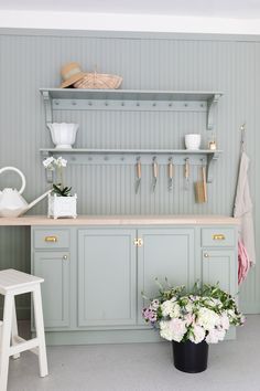 a kitchen with green cabinets and flowers on the counter top, along with a white stool