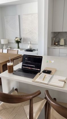 an open laptop computer sitting on top of a white table next to two brown chairs