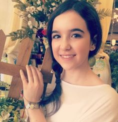 a woman holding up a wooden cross in front of a christmas tree