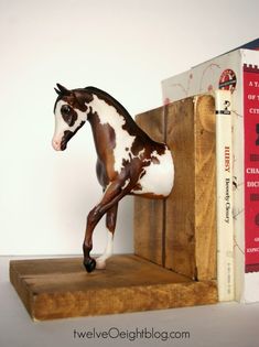 a horse figurine standing on top of a wooden shelf next to two books