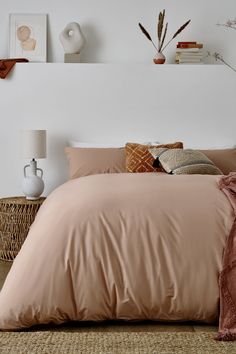 a bed with pink sheets and pillows in a white room next to a wicker basket