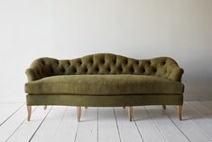 a green couch sitting on top of a wooden floor next to a white wall in an empty room