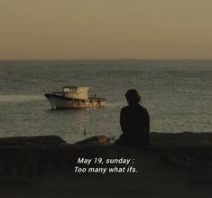 a person sitting on a rock looking out at the ocean with a boat in the distance