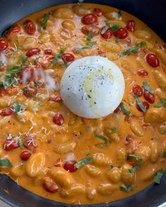 an egg on top of some pasta in a skillet with tomatoes and parsley