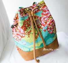 a multicolored floral print bag with brown leather handles and straps on a white background