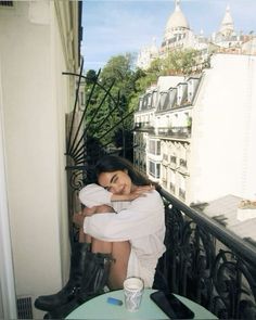 a woman sitting on top of a balcony next to a table with drinks in front of her