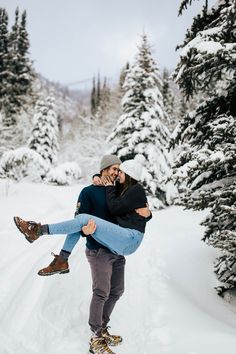 a man carrying a woman on his back through the snow in front of some trees