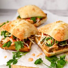 three sandwiches with meat and veggies are on wax paper next to a cutting board