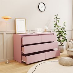 a pink dresser in a living room with a clock on the wall and plants next to it