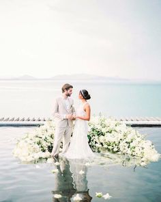 a bride and groom standing in the water with white flowers on it's side