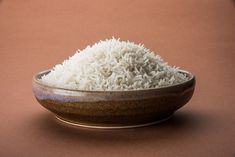 a bowl filled with white rice sitting on top of a brown table next to an orange wall