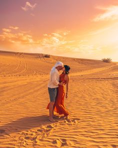 a man and woman standing in the sand at sunset