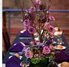 the table is set with purple napkins and flowers in a green vase on it