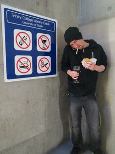 a man standing next to a sign holding a drink in his hand and eating food