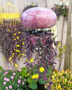 purple and yellow flowers are growing next to a birdcage in the garden with other plants