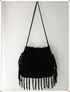 a black handbag hanging on a white wall with fringes and tassels