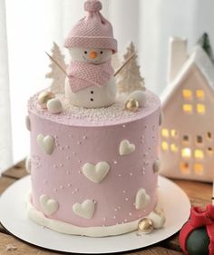 a pink frosted cake with a snowman on top and hearts around the edges