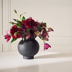 a black vase filled with lots of flowers on top of a white table next to a wall