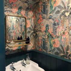 a sink and mirror in a small room with floral wallpaper on the walls behind it