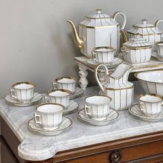 a table topped with lots of white and gold cups and saucers on top of a marble counter