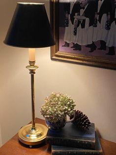 a table with a lamp and some books on it next to a framed painting in the corner