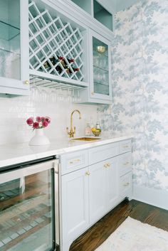 a kitchen with white cabinets and floral wallpaper on the walls, along with a gold faucet