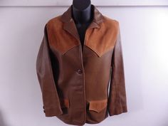 "Beautiful vintage leather jacket, in two-tone buckskin. Soft and supple tanned leather body with contrasting suede panels on the shoulders and pocket flaps. Fully lined in silky rayon. Two front buttons and two at each cuff. Very cute Western-style jacket, which would be perfect with jeans or a skirt. Jacket and lining are in excellent condition- very lightly worn. A tiny area of scratching on right shoulder- visible in last photo, but really minimal. Leather is amazingly soft and buttery- no stiffness or dry rot at all! Measurements: Bust: 33-34\" (marked 34) Waist: 32\" Sleeve length: 23\" Overall length (collar to hem): 28\"" Classic Brown Outerwear With Suede Overlays, Western Brown Fitted Leather Jacket, Fitted Brown Outerwear With Suede Overlays, Fitted Leather Jacket With Suede Overlays, Western Brown Outerwear For Work, Western Style Leather Jacket For Workwear In Winter, Brown Leather Jacket With Suede Overlays, Retro Brown Leather Blazer, Buckskin Jacket