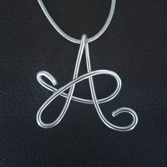 a silver necklace with the letter a in it's center on a black leather surface