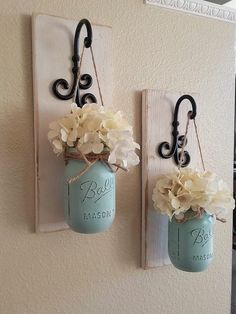 two mason jars with flowers are hanging on the wall next to hooks that hold them