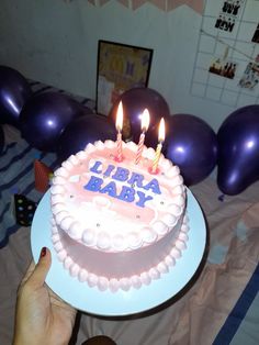 a birthday cake with lit candles sitting on top of a table next to purple balloons