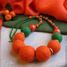 an orange and green beaded necklace on a white cloth with other items in the background