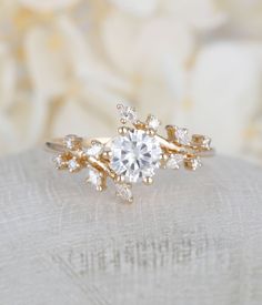 a close up view of a diamond ring on a white cloth with flowers in the background