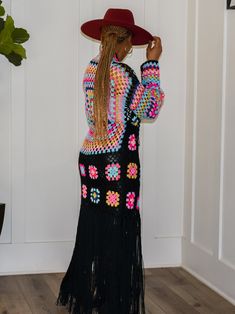 a woman in a colorful dress and hat is standing by the door with her hand on her hip