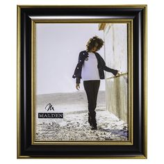 a black and gold framed photograph of a woman walking on the beach with her hand in her pocket