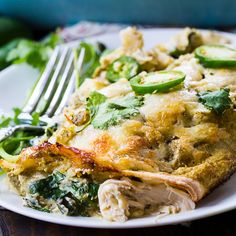 a white plate topped with lasagna covered in meat and veggies next to a fork