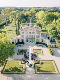 an aerial view of a large white house surrounded by greenery and trees with people standing in the front yard