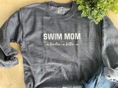 a gray sweatshirt with the words swim mom printed on it next to some green plants