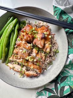 a white plate topped with meat and rice next to green beans on a tablecloth