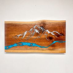 a piece of wood with mountains on it and blue water painted on the bottom part