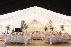 the inside of a tent with tables and chairs set up for a formal function in white linens