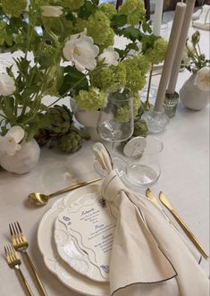 a table set with place settings and flowers in vases on the side, along with silverware