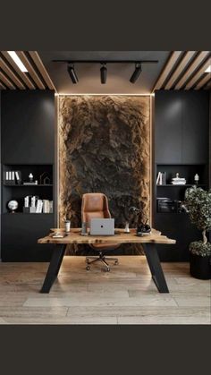 a desk with a laptop on it in front of a large stone wall and shelves