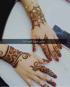 two hands with henna designs on them, one has red nails and the other has gold