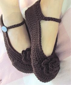 a woman's feet wearing brown crocheted slippers with a flower on the side