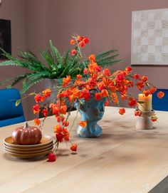 an arrangement of orange flowers in a blue vase on a wooden table with plates and candles