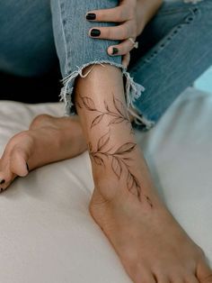 a woman's leg with a tattoo on it and her nails painted black, sitting on a bed