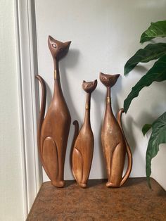 three wooden cats sitting on top of a table next to a potted green plant