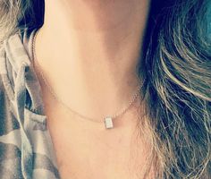 a woman wearing a silver necklace with a square shaped pendant on it's neck